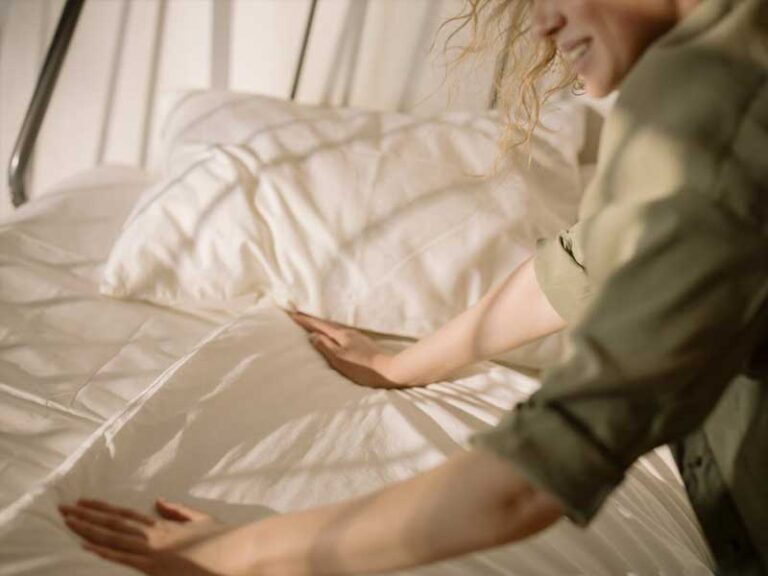 A Lenuma cleaner gently smoothing a freshly made bed with crisp white linens, creating a calm, welcoming bedroom space.