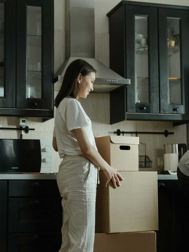 A woman in a clean, minimalist kitchen preparing moving boxes, reflecting Lenuma’s thoughtful and respectful moving cleaning service.