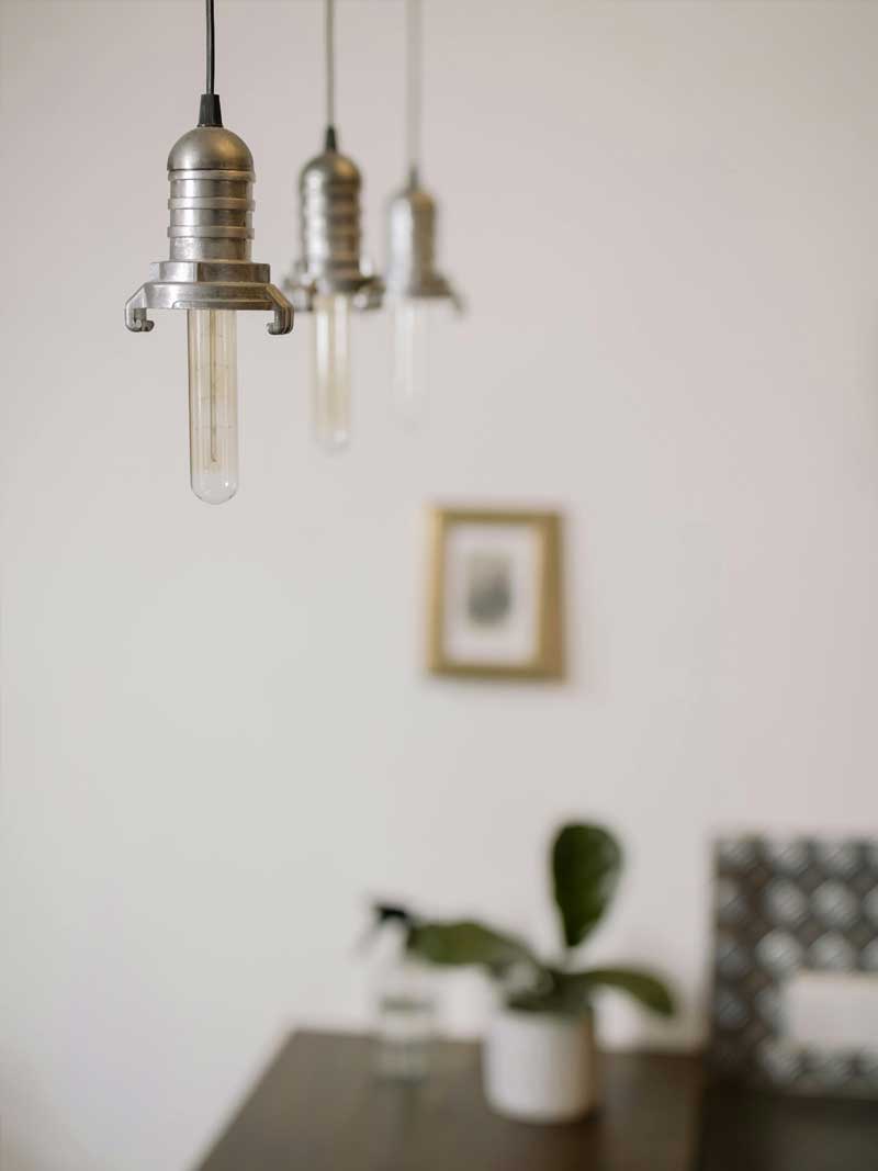 Warm minimalist hanging lights above a tidy, plant-accented table, evoking Lenuma’s calm, cared-for home atmosphere.