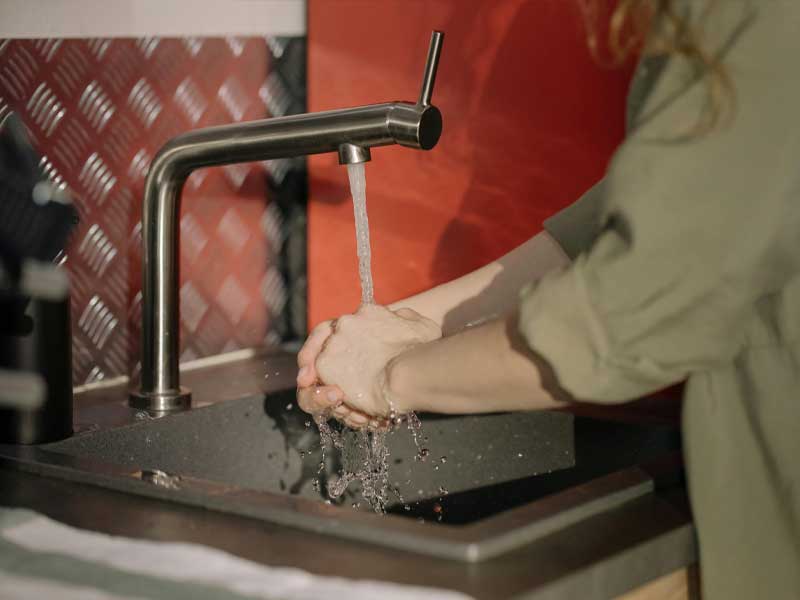 A home care professional washing hands at a kitchen sink, reflecting cleanliness, hygiene, and respect for the spaces Lenuma cares for.